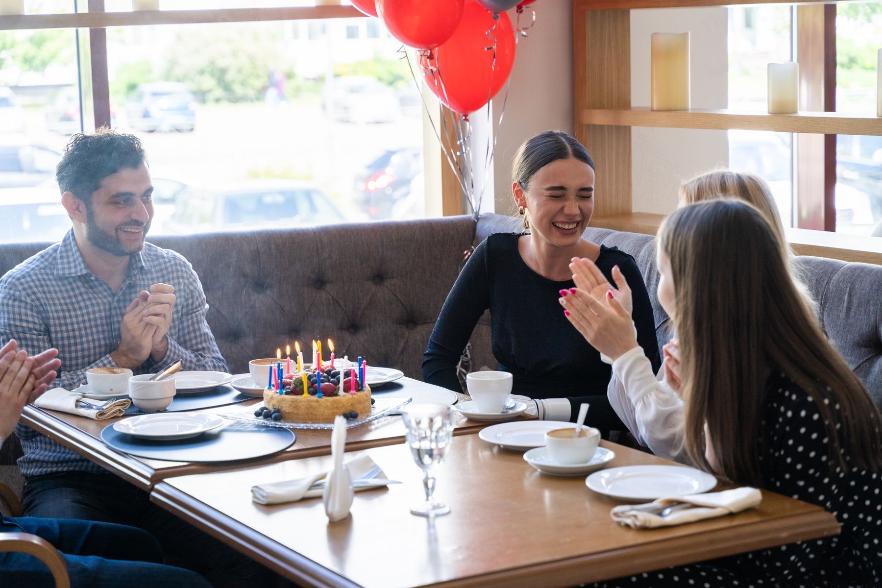 A group around a table in a private room, clapping over a cake and balloons