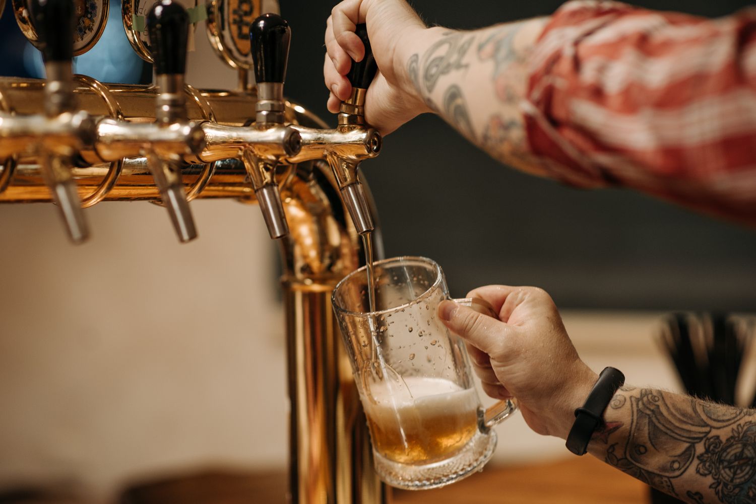 A bartender pulling a glass of draught beer from a brass tap